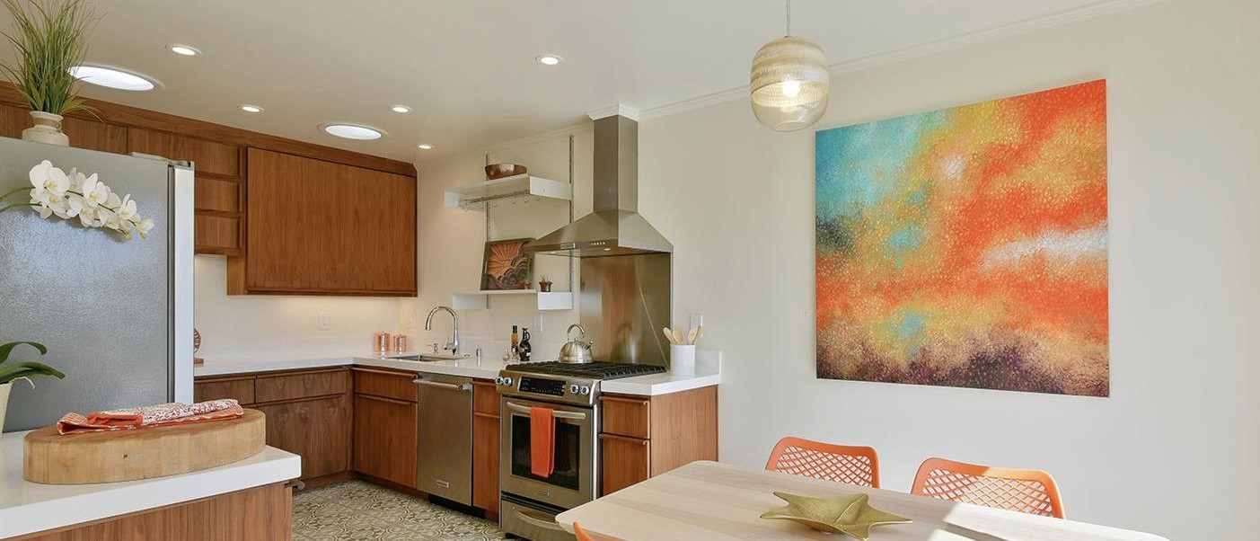Kitchen with custom built cabinets, solar-tube skylight, orange chairs and bold orange artwork by Katja Francesca Tapia.