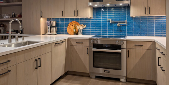 Kitchen with Stainless Steel Range, iridescent blue tile and light wood cabinetry