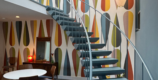 Dramatic sweeping staircase in two story great room with wallpaper.